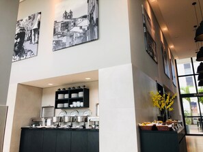 Ein moderner Küchenbereich mit einer Kaffeestation, Schwarzweißkunst an den Wänden und Blick ins Freie durch große Fenster.