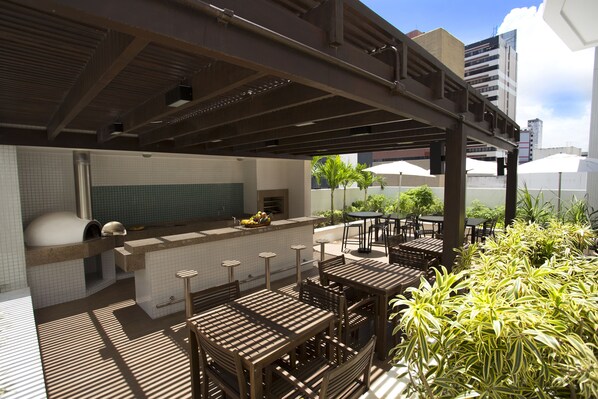 Eine Außenpatio-Terrasse mit Holztischen und -stühlen, eine Bar mit Theke und Hockern sowie Kübelpflanzen.