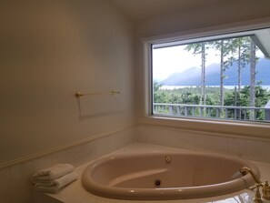 Ein Badezimmer mit einer Badewanne, einem Fenster mit Blick auf Bäume und Berge sowie einem Handtuchhalter.