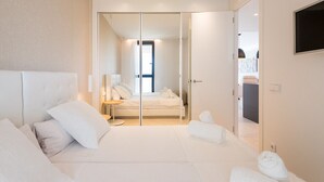Una habitación de hotel moderna con una cama grande, un separador de vidrio y un televisor montado en la pared.