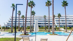 Un área de piscina con dos sillas de descanso, una sombrilla blanca y palmeras.