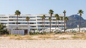 Un hotel de varios pisos, con palmeras y montañas al fondo.