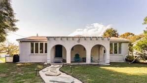 A white building with a stone facade, three arched doorways, and a covered porch area.