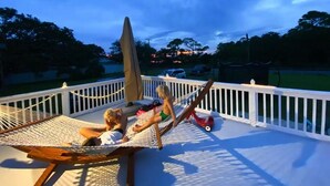 A hammock on a deck with a view of a sunset over a body of water.