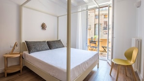 A bedroom with a four-poster bed, a small bedside table, a chair, and a view of the outside balcony. - Le Niche Holiday Home - Balcony by Wonderful Italy (Palermo)