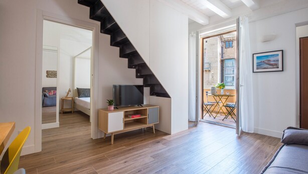 A modern living room with a wooden floor, a staircase, a TV on a wooden stand, and a balcony with a view. - Le Niche Holiday Home - Balcony by Wonderful Italy (Palermo)