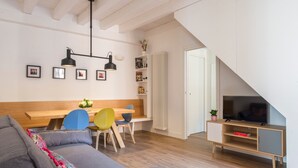 A modern living room with a sofa, a dining table, chairs, a TV, and a staircase. - Le Niche Holiday Home - Balcony by Wonderful Italy (Palermo)