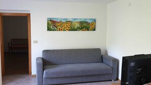A living room with a grey sofa, a painting on the wall, and a television on the right.