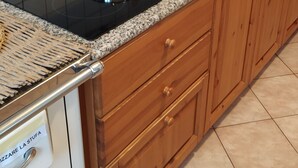 A kitchen with a black stovetop, stainless steel sink, wooden cabinets, and white tiled backsplash.