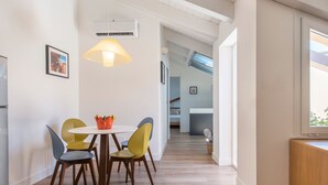 A modern kitchen with a dining area, featuring a white table with colorful chairs, a hanging lamp, and a view of the adjacent living space. - Le Niche Holiday Home - Terrace by Wonderful Italy (Palermo)