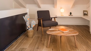 A modern living room with a dark grey armchair, a round wooden coffee table, and a small side table with a lamp and books. - Le Niche Holiday Home - Terrace by Wonderful Italy (Palermo)