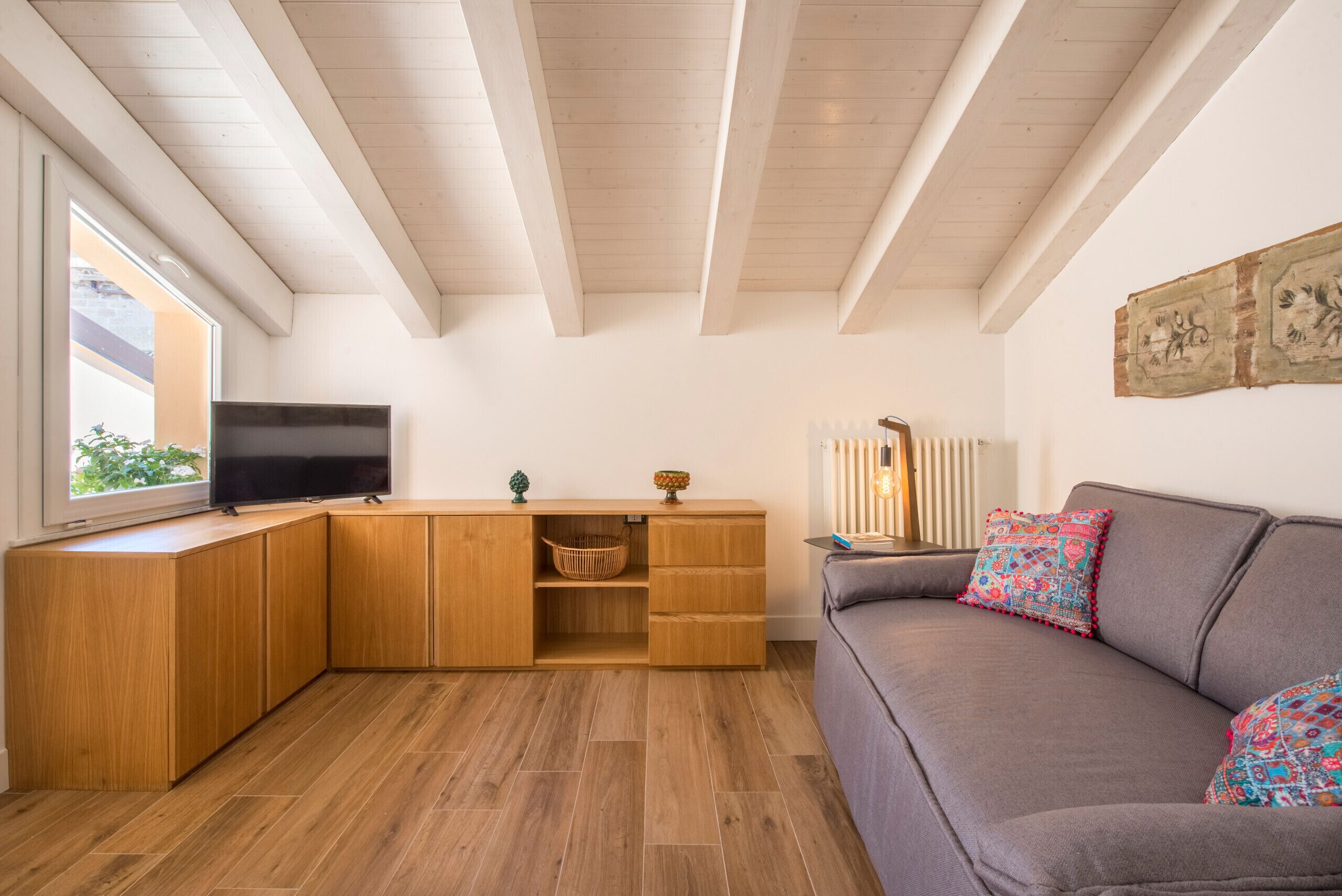Una sala moderna con un mueble de madera, un televisor, un sofá y una ventana.