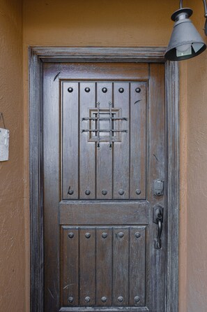 Uma porta de madeira com uma tranca de metal e uma fechadura, embutida em uma parede bege.