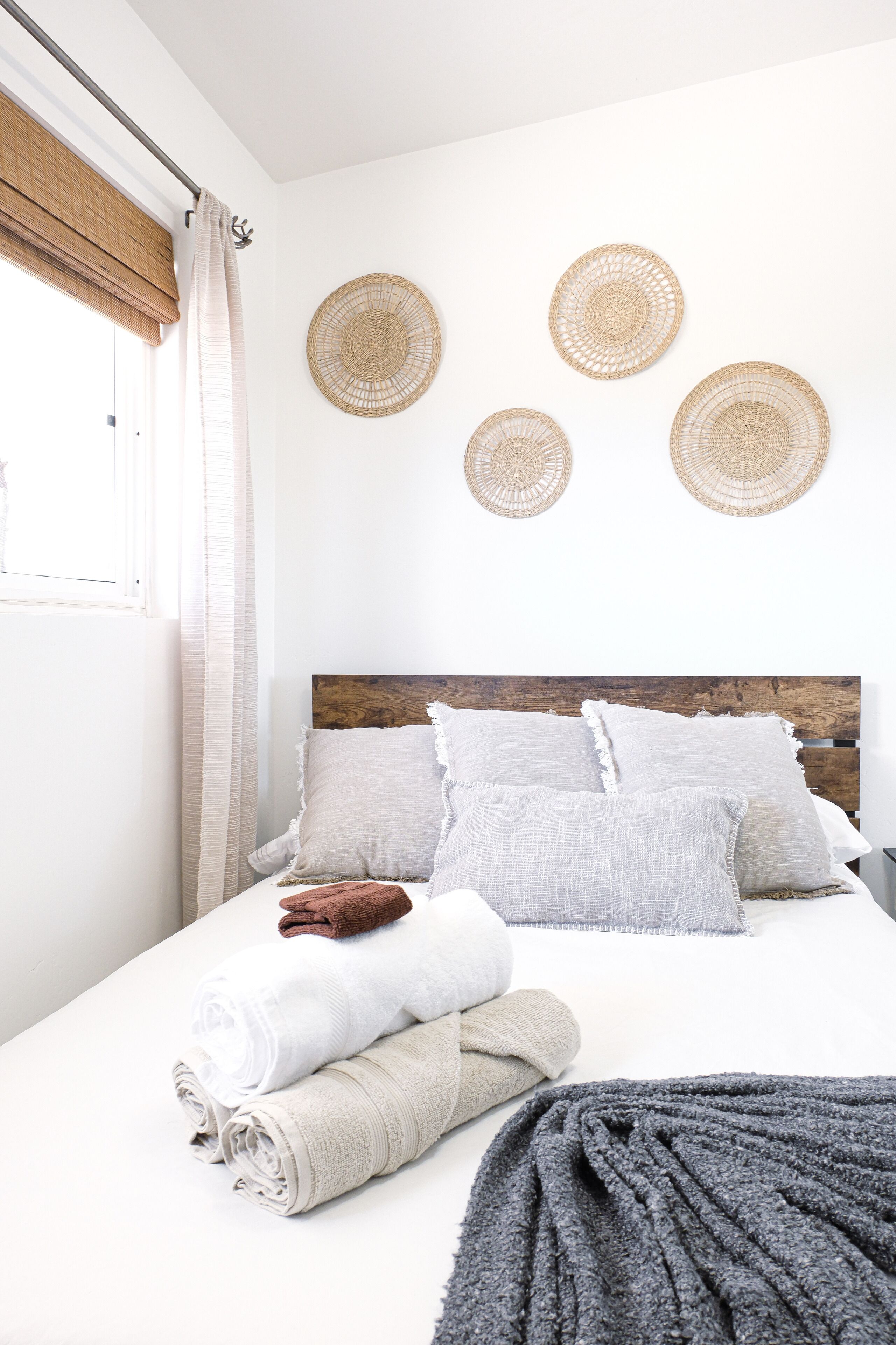 A neatly made bed with rolled towels, a grey throw blanket, and a wooden headboard.