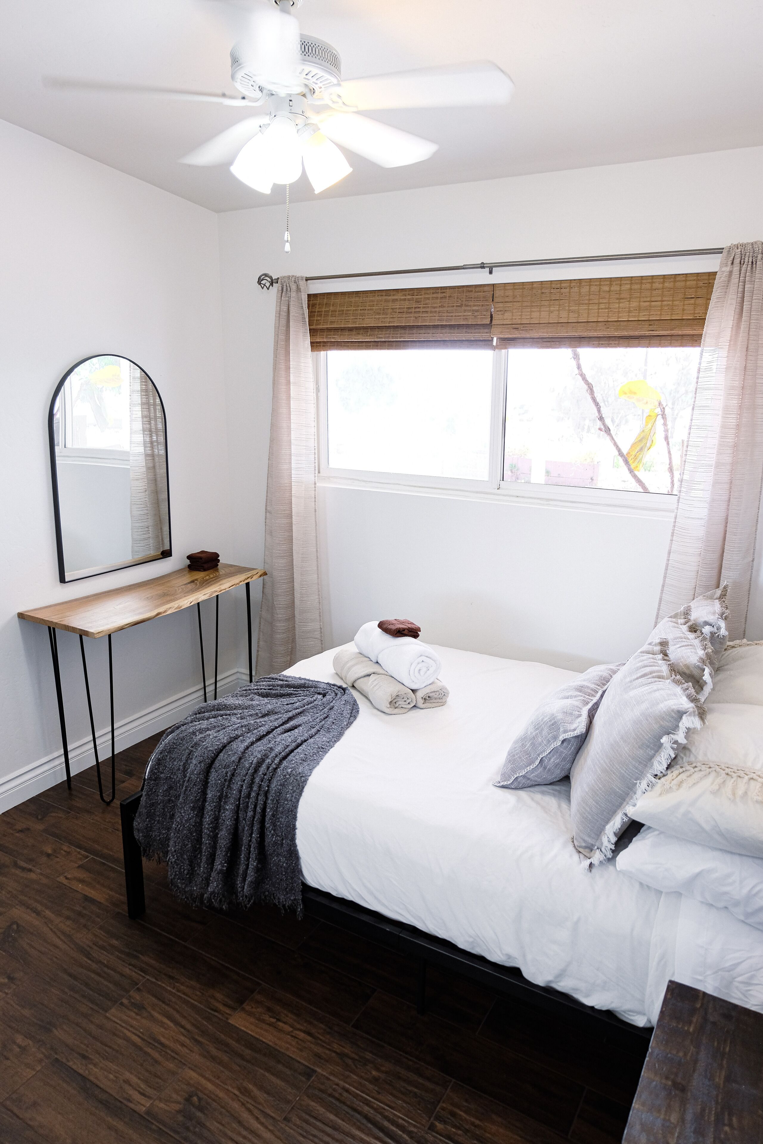 Un dormitorio con cama, mesita de noche, espejo y ventana con cortinas.