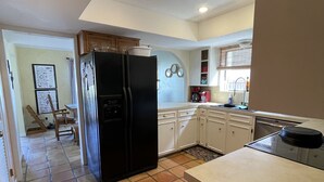 A kitchen with a black refrigerator, white cabinets, a tiled floor, and a window with blinds. - North Padre Island waterfront canal  home w/private dock and pool (Corpus Christi)