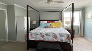 A four-poster bed with a floral bedspread, a ceiling fan, and a nightstand with a lamp. - North Padre Island waterfront canal  home w/private dock and pool (Corpus Christi)