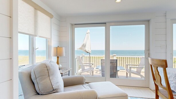 Une pièce dotée d’une grande porte-fenêtre coulissante donnant sur un balcon avec vue sur la plage, un coin salon confortable et une table avec un parasol.