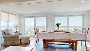 A dining area with a view of the sea, a table set with plates and glasses, and a bench.
