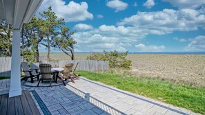 Une terrasse avec des fauteuils Adirondack et une table, donnant sur un champ verdoyant et une plage.