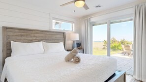 Une chambre à coucher avec un grand lit, une tête de lit en bois, une table de chevet avec une lampe, et une vue sur l’extérieur.
