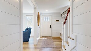 Un couloir avec un plancher en bois, une porte blanche, une chaise bleue et un escalier avec une rampe rouge.