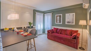 A modern living room with a red sofa, a dining table with breakfast items, and a large window with curtains. - Lo Squero 2 Charming Apartment in Dorsoduro (Venice)