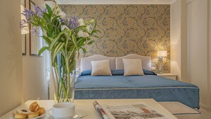 A hotel room with a bed, a bedside table with a cup of coffee, a plate of pastries, and a newspaper. - Lo Squero 2 Charming Apartment in Dorsoduro (Venice)