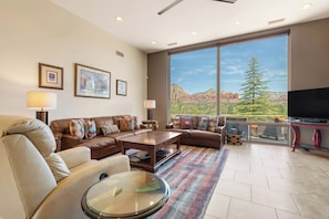 A spacious living room with a large window, a sofa set, a coffee table, and a flat-screen TV.