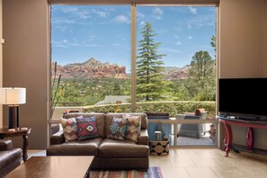 Un salon avec une grande fenêtre, un canapé, un téléviseur et une vue sur les montagnes.