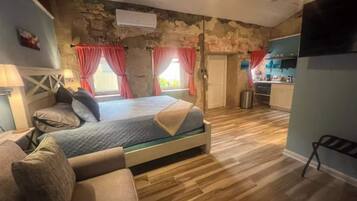 Ein Schlafzimmer mit Bett, Sofa, Steinwand und Küchenzeile.