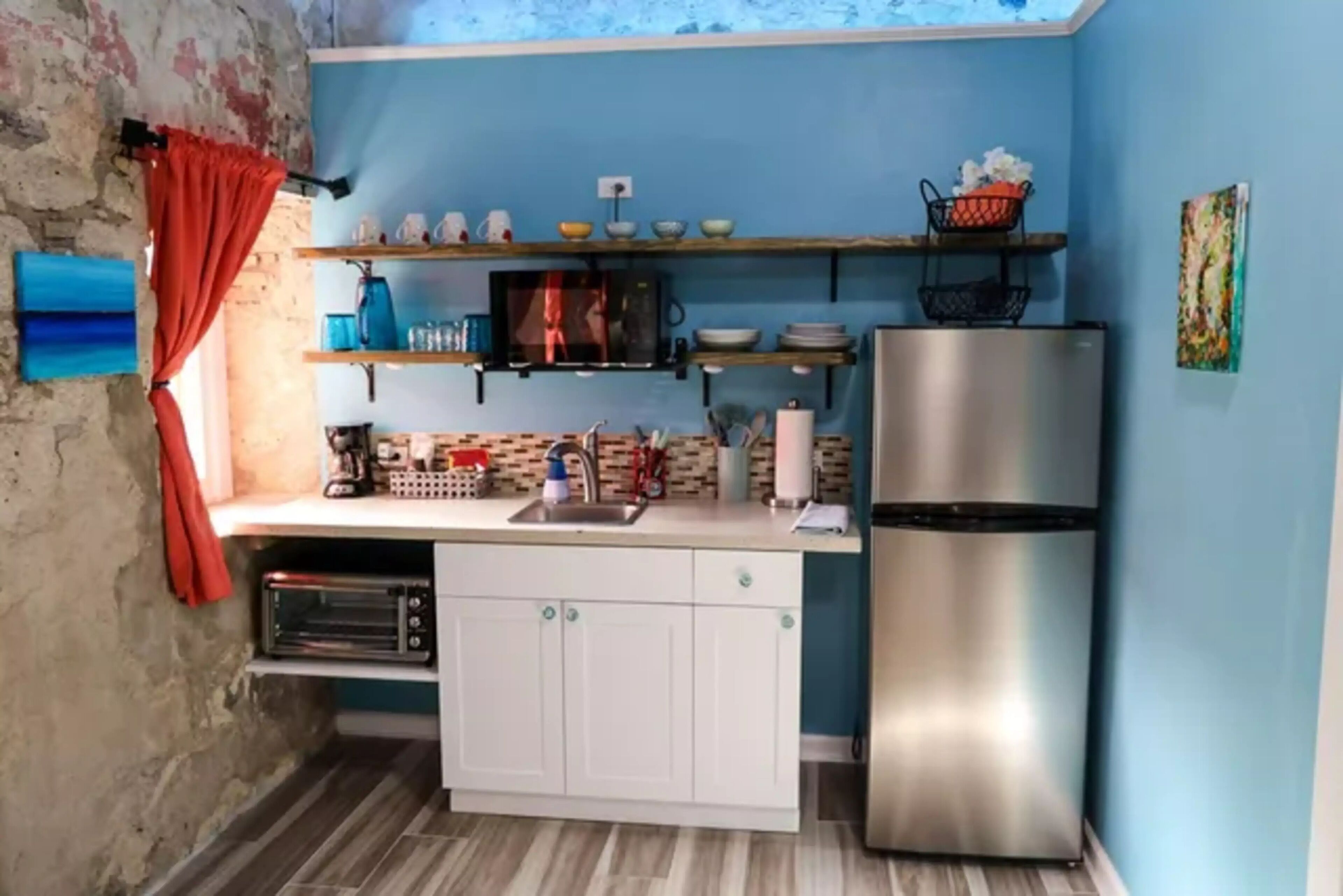 A compact kitchen with white cabinets, a stainless steel refrigerator, and a microwave on a shelf.