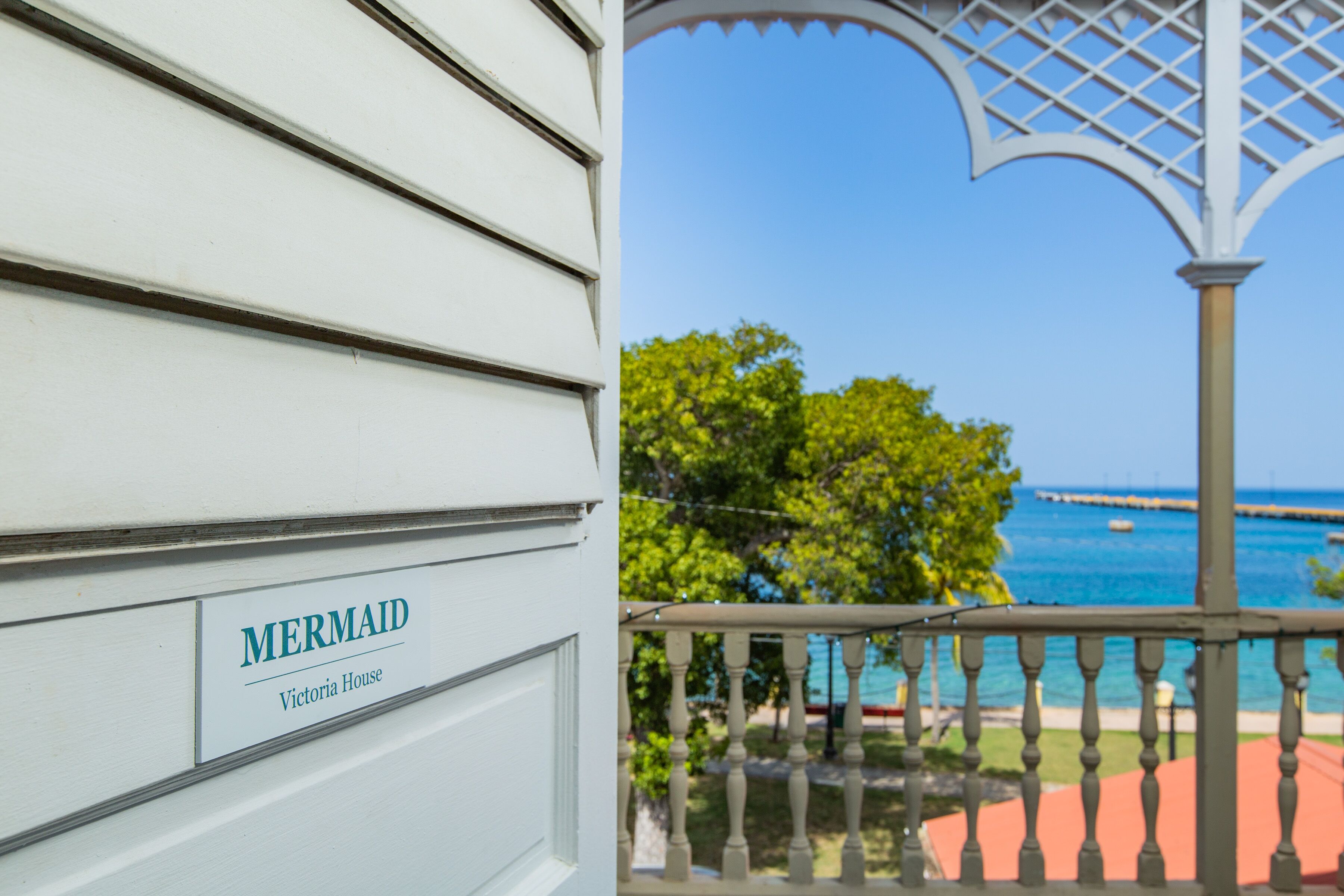 Un bâtiment blanc avec une enseigne indiquant « MERMAID Victoria House » et un balcon offrant une vue sur la mer et un quai.