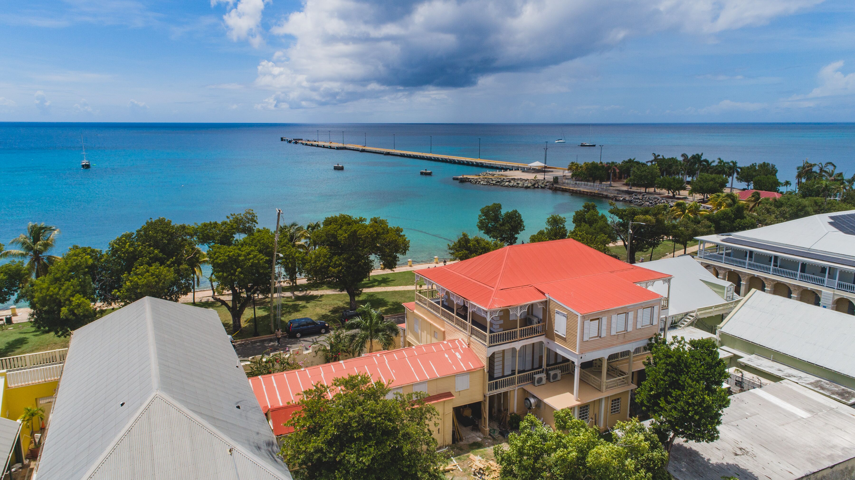 A coastal view with a pier extending into the sea, surrounded by buildings with red roofs and balconies.