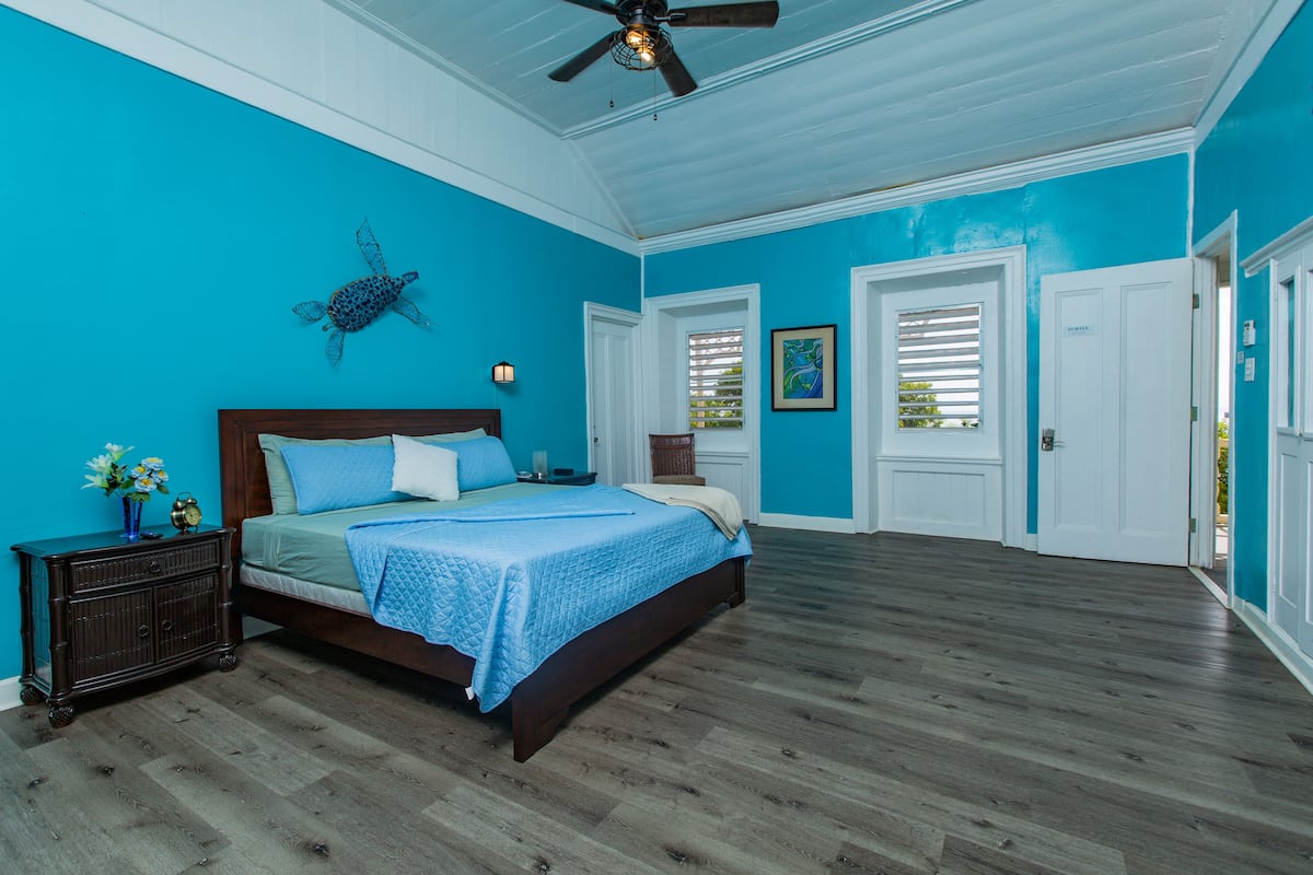 A bedroom with a large bed, a ceiling fan, and a view of the outdoors through a window.