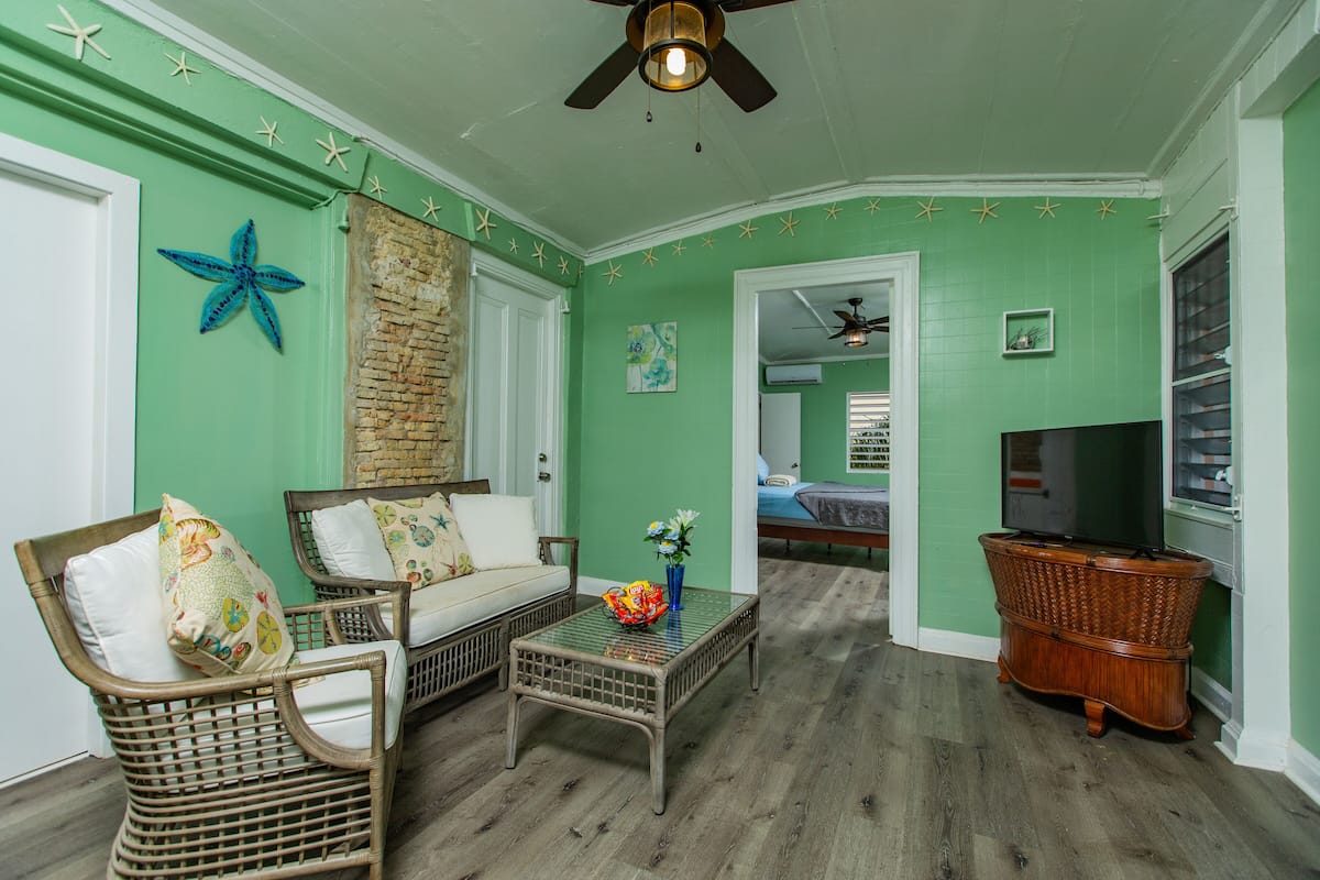 A room with a green wall, wicker furniture, a glass coffee table, and a television.