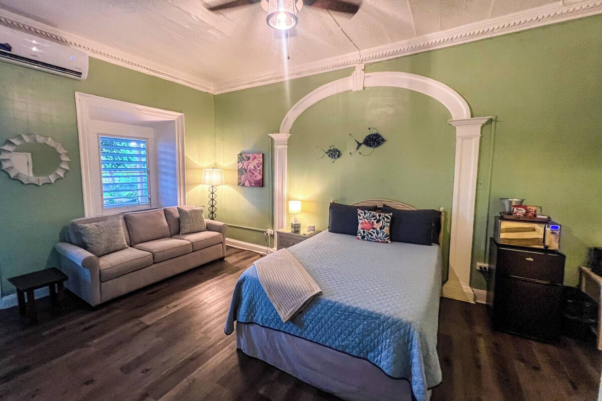 A bedroom with a bed, a sofa, a ceiling fan, and a window with blinds.