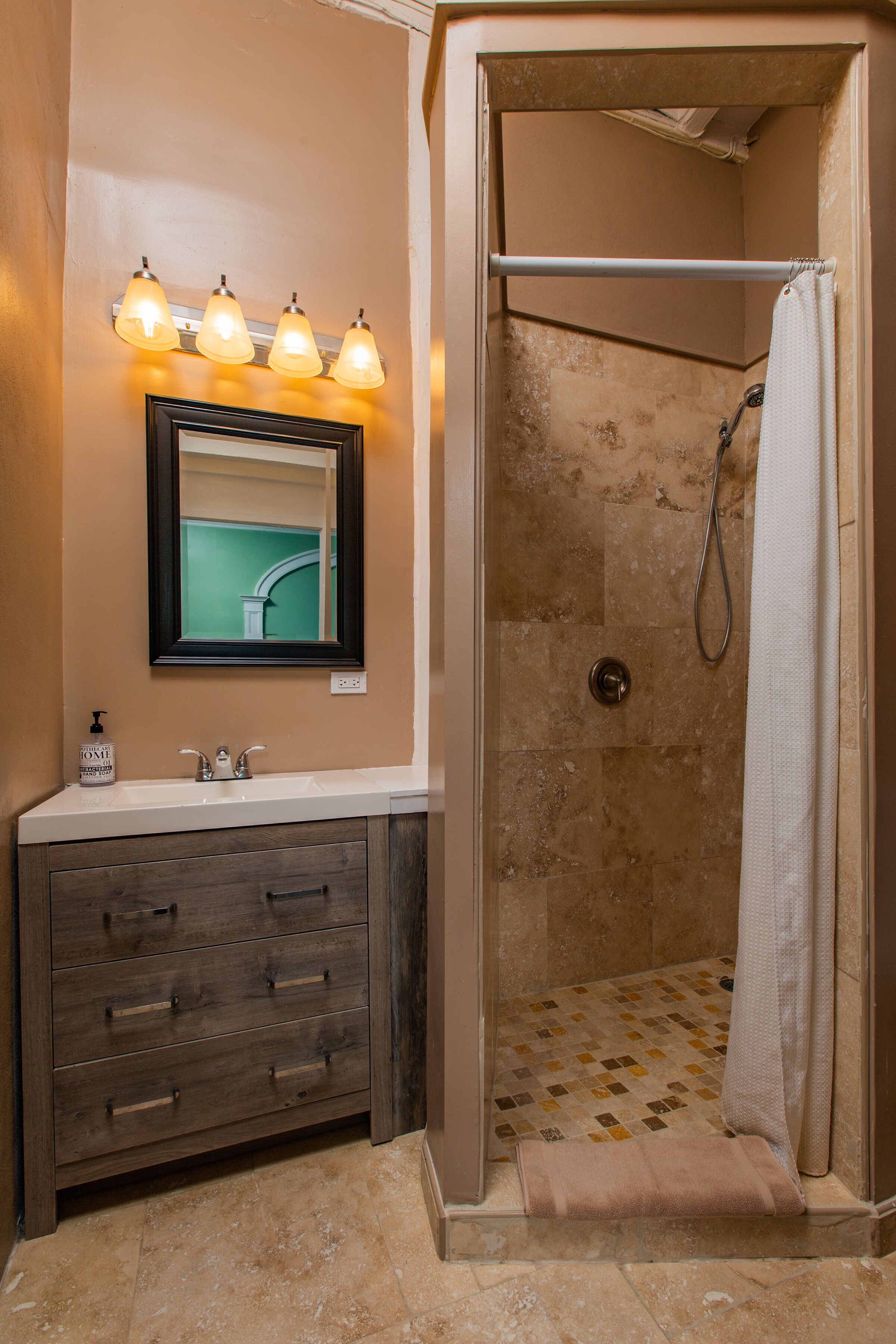 Un baño con ducha, un lavabo con espejo y un perchero para toallas.