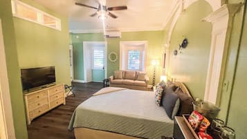 A bedroom with a bed, a television, a ceiling fan, and a dresser.
