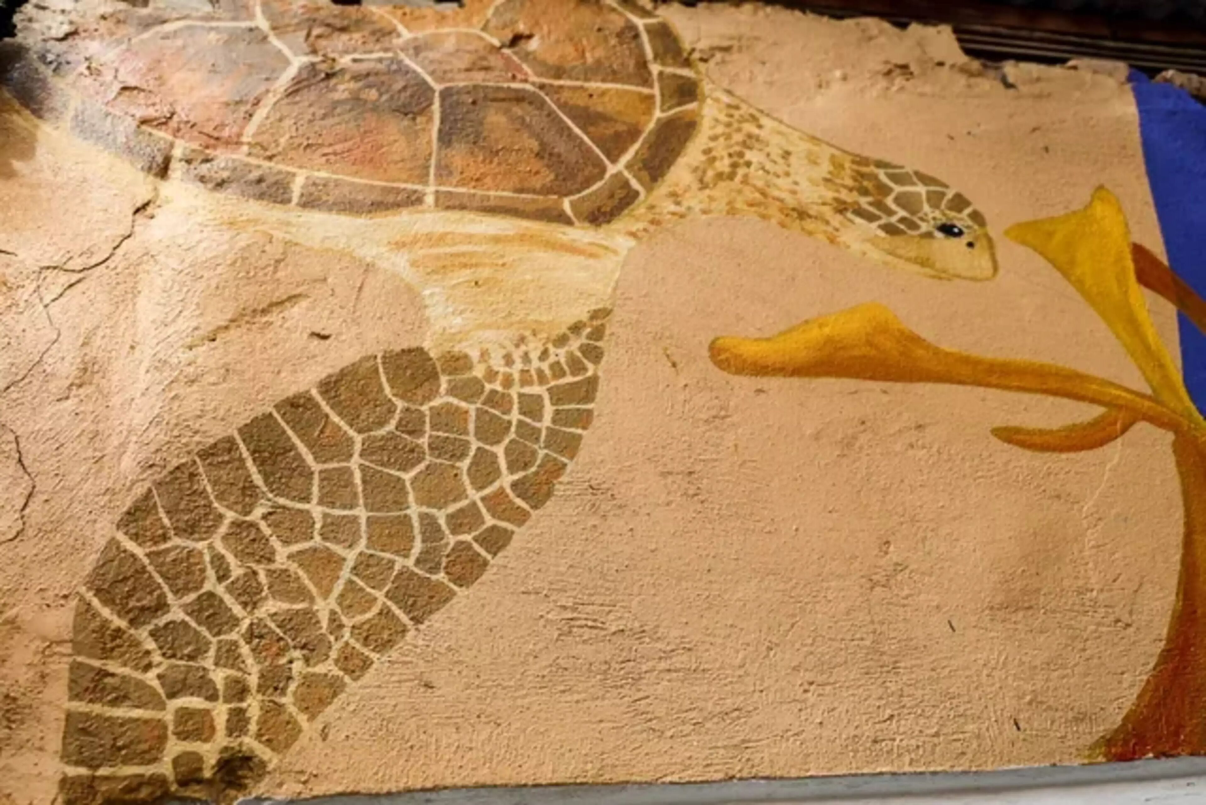 A mosaic of a sea turtle on a textured wall.