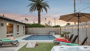 Un jardin avec une piscine, des chaises longues, un jacuzzi et des guirlandes lumineuses.