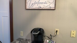 Una cafetera sobre una encimera de granito, con un soporte para cápsulas de café debajo.
