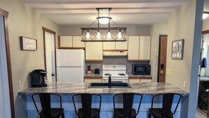 Una cocina con una isla central, taburetes de bar, un refrigerador, un microondas y una estufa.