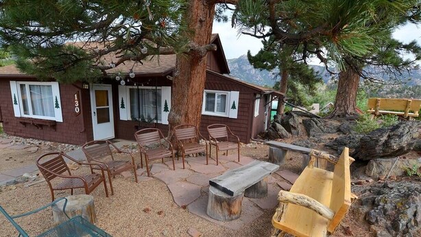 Una cabaña rústica con un patio de piedra, muebles de madera y un banco hecho con troncos de árbol.