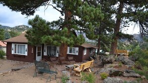 Una cabaña rústica con un patio, mobiliario exterior y un árbol grande al frente.