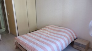 Een eenpersoonsbed met een gestreept beddegoed, een houten nachtkastje met lades en een ventilator aan de muur.
