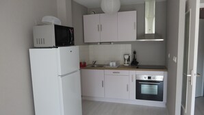 Een compacte keuken met witte kastjes, een magnetron, een koffiezetapparaat en een vaatwasser.