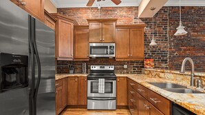 A kitchen with wooden cabinets, a stainless steel refrigerator, a microwave, an oven, and a granite countertop. - The Johnny Cash Dual Condos Downtown at Printer's Alley & Steps to Broadway (Nashville)