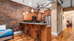 A modern kitchen with a brick wall, wooden cabinets, a central island with stools, and a ceiling fan. - The Johnny Cash Dual Condos Downtown at Printer's Alley & Steps to Broadway (Nashville)