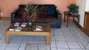 A reception area with a sign reading "EXECUTIVE INN & SUITES," a brown sofa, a coffee table with magazines and a book, a vase with flowers, and a chandelier. - Executive Inn and Suites (Mission)